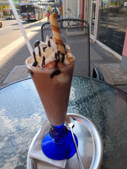 A cup of iced chocolate, nicely decorated with whipped cream and a kind   of cookie.