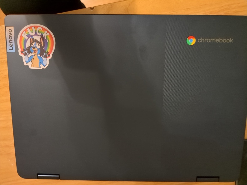 A Chromebook, closed, located on a table. There is s a furry sticker on it